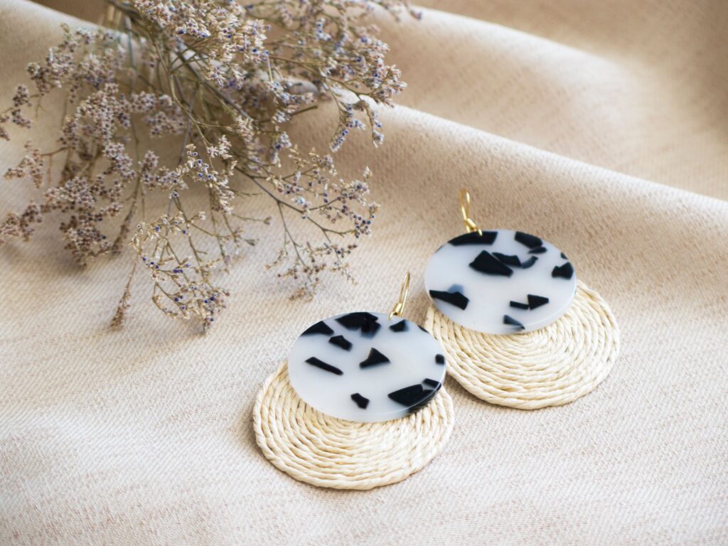 Stylish black and white statement earrings displayed with dried flowers on a beige fabric backdrop.