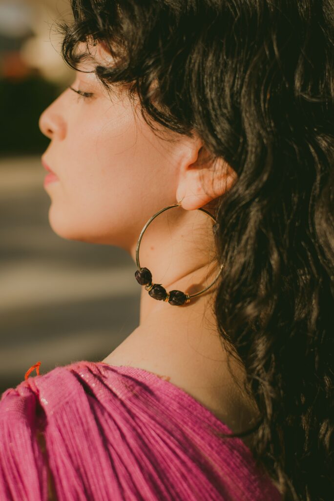 Profile of a woman in a pink outfit showcasing elegant hoop earrings in a soft outdoor setting.